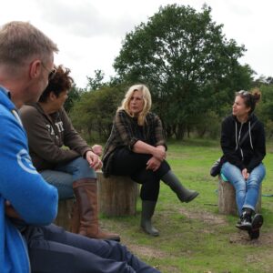 4 personen zitten met elkaar in gesprek op boomstammen midden in het duingebied van het Nationaal Park Zuid Kennemerland, zij zijn buiten aan het vergaderen en zitten er ontspannen bij