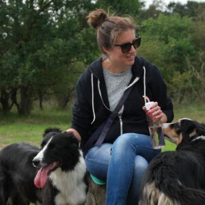 Iris zit op een boomstronk in het Nationaal Park Zuid Kennemerland en knuffelt met de honden van de schaapskudde